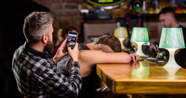 Hipster tomando fotos borracho amigo. Amigos borrachos en el bar. Duerme en el mostrador del bar. Toma una foto para recordar la fiesta. Hipster burlándose de un amigo borracho. Hombre borracho se duermen y chico con smartphone —  Fotos de Stock