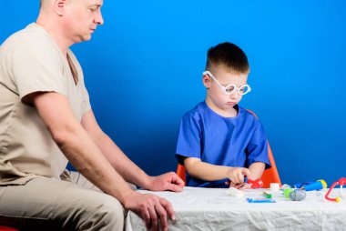 Hastalık tedavisi. Baba ve oğul tıbbi hanedan. Tıbbi muayene. Çocuk sevimli çocuk ve babası doktor. Hastane çalışanı. Sağlık. Tıp kavramı. Çocuk küçük doktor masa tıbbi araçları oturup