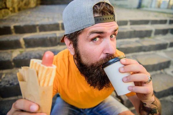 Bebe algo diferente. hipster caucasiano gosta de beber bebida takeaway com cachorro-quente. Homem barbudo tomando um gole de café fresco na xícara descartável. Alimentos e bebidas nutricionais — Fotografia de Stock