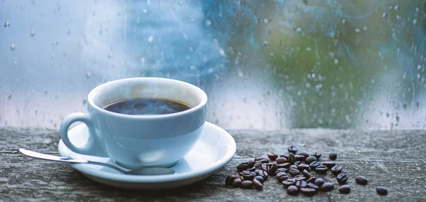 Kaffee genießen an regnerischen Tagen. Kaffee-Morgenritual. frisch gebrühter Kaffeebecher und Bohnen auf der Fensterbank. feuchtes Glasfenster und eine Tasse heißen Kaffee. Herbst trübes Wetter besser mit Koffeingetränk — Stockfoto