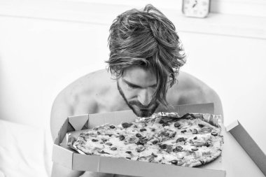 Gıda teslim Servisi. Bir yatağa evde döşeme sırasında tembel kaslı adam yeme pizza portresi. Adam yakışıklı adam yatakta kahvaltı için peynirli yemek yeme sakallı. Pizza yatak.