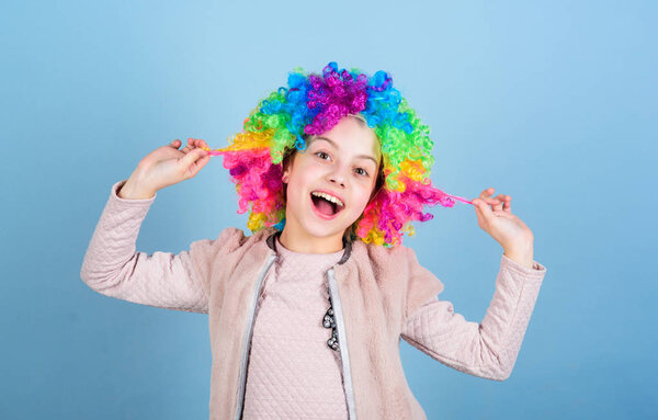 Playing with her hair. Funny kid with curly synthetic hair. Cute little girl with fancy hair. Adorable small child wearing bright clown hair wig