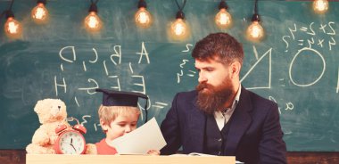 Öğretmen, babası ödev, kontrol yardımcı olur çocuk için evlat. Bireysel eğitim kavramı. Meşgul bir çocuk okulda okuyor. Öğretmen formal giyim ve öğrenci sınıfta kolej, kara tahta arka plan