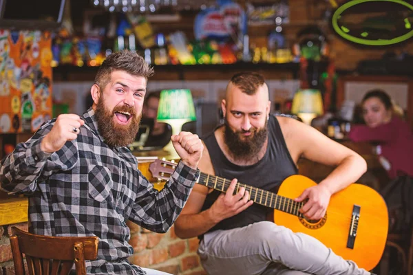 Cheerful friends sing song guitar music. Relaxation in pub. Friends relaxing in pub. Live music concert. Man play guitar in pub. Acoustic performance in pub. Hipster brutal bearded with friend in pub