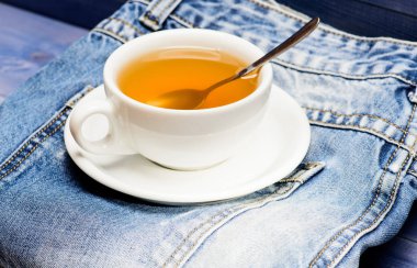 Sağlıklı alışkanlıklar. Çay saati konsepti. Fincan bardağı sıcak su ve çay torbası. İşlem çay seramik kupa demleme. Bitkisel yeşil veya siyah bütün yaprak. Kupa dolu kaynar su ve çay poşeti mavi kot arka plan üzerinde