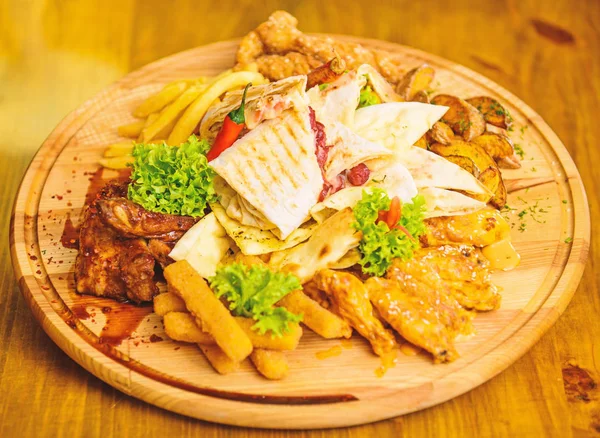 Meat snack for group friends. Tasty delicious snacks. Restaurant food. Snack for beer. Wooden board french fries fish sticks burrito and meat steak served with salad. Enjoy your meal. Pub menu snack