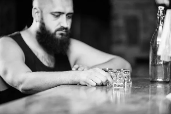 Hipster brutal man drinking alcohol ordering more drinks at bar counter. Alcoholism and depression. Guy spend leisure in bar with alcohol. Man drunk sit alone in pub. Alcohol addicted concept