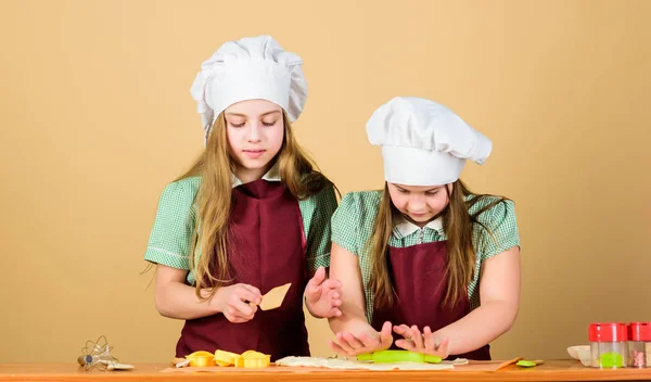 Grembiuli per bambini e cuoco cappelli da cucina. Biscotti fatti in casa meglio. Ricetta di famiglia. Abilità culinarie di cucina. Cucinare biscotti allo zenzero. Ragazze sorelle divertirsi pasta allo zenzero. Bambini che cucinano biscotti insieme — Foto Stock