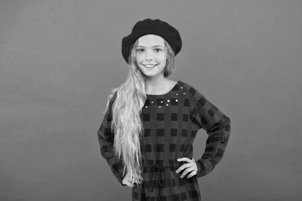 Bära basker som mode flicka. Kid söta lilla flicka med långa blonda hår poserar i basker hatt och rutig klänning röd bakgrund. Fashionabla beret tillbehör för kvinna. Beret stilinspiration — Stockfoto