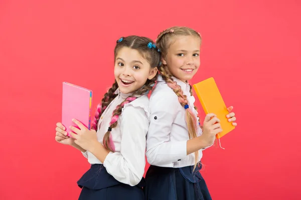 Ces livres sont absolument géniaux. Des petits enfants géniaux souriant sur fond rouge. Filles de génie heureux ou des enfants émerveillés avec des livres. Petites écolières tenant des livres avec des idées de génie — Photo