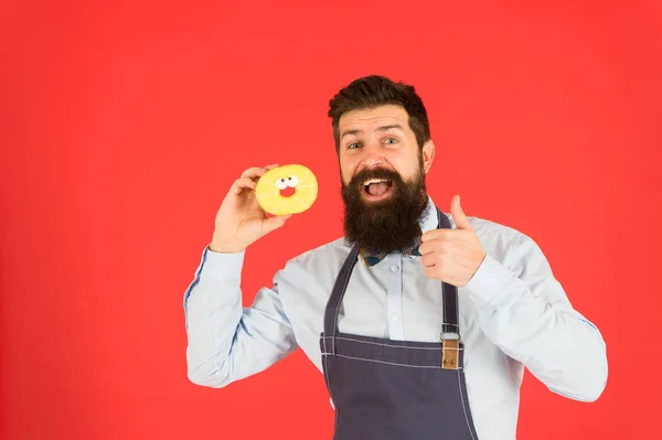 Homem barbudo e bem preparado com avental a vender donuts. Comida de donut. O padeiro Hipster segura donuts. Humor alegre. Calorias de donut. Donut vitrificado. Produtos de panificação. Doces e bolos. Comida de plástico. Dieta de glúten de carboidratos — Fotografia de Stock