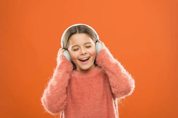 Bom som. Menina bonito criança usar fones de ouvido ouvir música. Miúdo ouvir música fundo laranja. Música recomendada com base no interesse inicial. Melhores aplicativos de música gratuitos para o seu dispositivo móvel — Fotografia de Stock