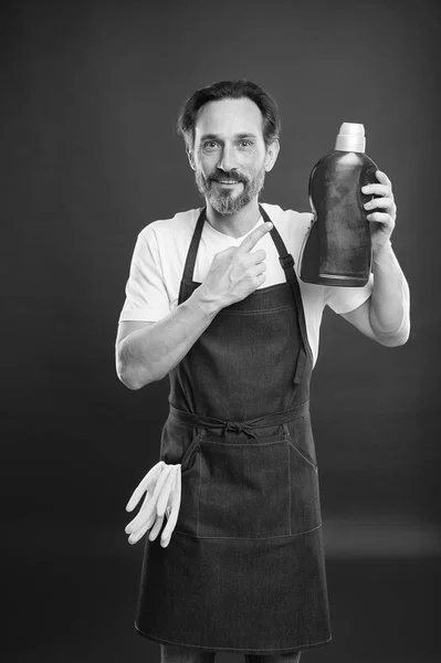 On guard of cleanliness and order. Cleaning service and household duty. Man in apron with gloves hold plastic bottle liquid soap chemical cleaning agent. Cleaning day today. Bearded guy cleaning home — Stock Photo, Image