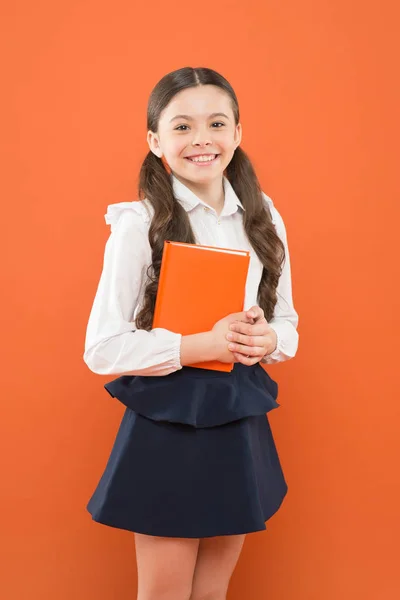 Школярка пише нотатки на помаранчевому тлі. маленька дівчинка в шкільній формі. читання уроку. інформаційна форма книги. повернутися до школи. щаслива дитина зосереджена на роботі. Урок у школі. Розумна дівчина школи — стокове фото