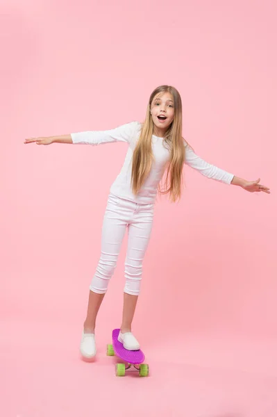 Opnieuw genereren van haar energie skateboarden. Schattig klein kind het uitvoeren van skateboarden trucs op roze achtergrond. Schattig klein meisje skateboarden op Violet Penny Board. Ga skateboarden dag — Stockfoto