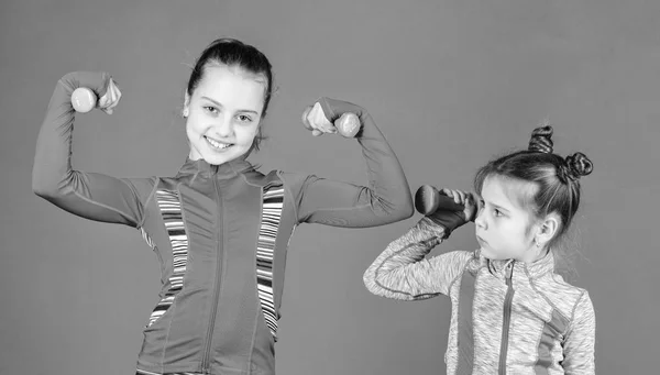Girls cute kid exercising with dumbbells. Motivation and sport example concept. Toddler repeat exercise after sister. Sport exercises for kids. Healthy upbringing. Sporty babies. Following her sister