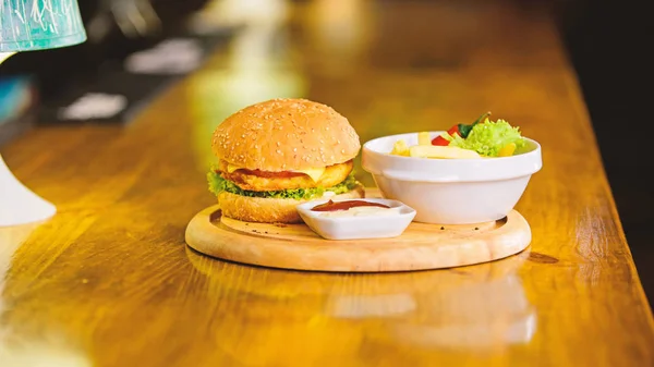 Delicious burger with sesame seeds. Burger with cheese meat and salad. Fast food concept. Burger menu. High calorie snack. Hamburger and french fries and tomato sauce on wooden board. Cheat meal