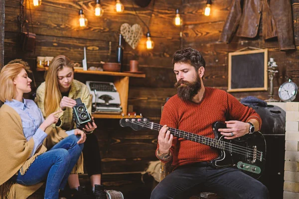 Hombre con barba larga disfrutando de la música. Músico con la cara tranquila y concentrada tocando para su esposa e hija. Mamá ayudando a la adolescente a lidiar con la cámara retro. Hombre barbudo afinación guitarra eléctrica — Foto de Stock