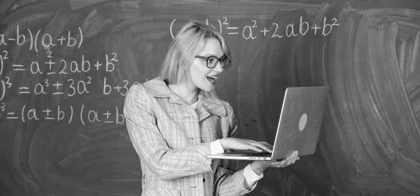 Educator smart clever lady with modern laptop searching information chalkboard background. Learn it easy way. Online schooling concept. Woman teacher wear eyeglasses holds laptop surfing internet Royalty Free Stock Images