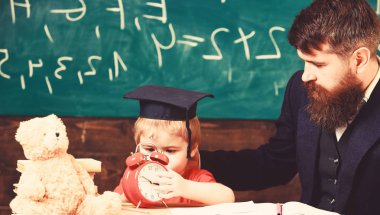 Evlat, öğretmen çocukla konuşurken çalar saat çocuk sakin yüz tutar. Bireysel ders kavramı. Sakallı öğretmen, babası sınıfta, arka plan kara tahta küçük oğlu öğretir.