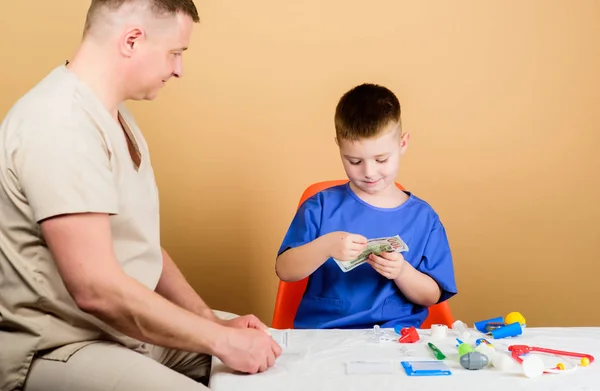 Salary of hospital worker. Boy cute child and his father doctor. Medical help. Medical insurance. Medicine concept. Kid little doctor sit table medical tools. Health care. Medical examination — Stock Photo, Image