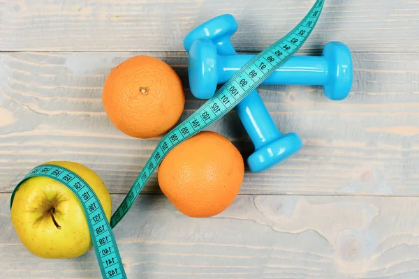 Gezondheid en sportschool concept, halters gewicht met meetlint, fruit — Stockfoto