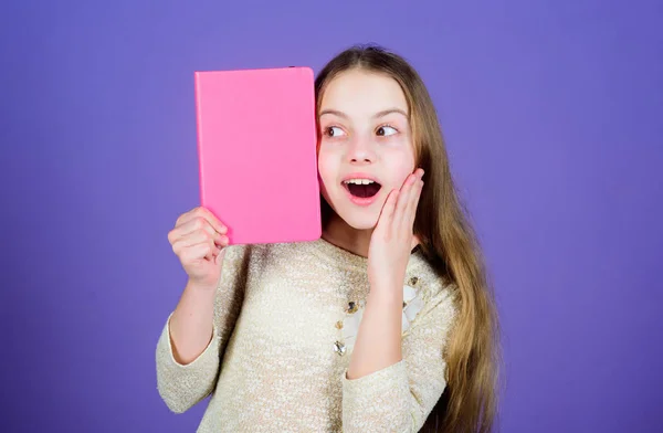 Melhorar-se através da educação. Menina surpreendida com boca aberta segurando livro de educação com capa rosada. Criança pequena bonito recebendo educação formal na escola primária. Educação, espaço de cópia — Fotografia de Stock