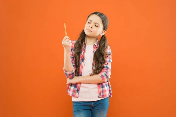 Serieuze gedachte. Klein schattig kind denken over idee met een zorgvuldige gedachte op oranje achtergrond. Genie meisje verloren in gedachten te kijken naar pen. Het geeft haar stof tot nadenken — Stockfoto