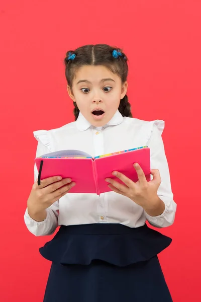 真是个意外的消息。惊讶的女孩阅读红色背景的书。可爱的小孩与惊喜的情感在脸上。可爱的小女孩张嘴大惊喜。惊喜理念 — 图库照片