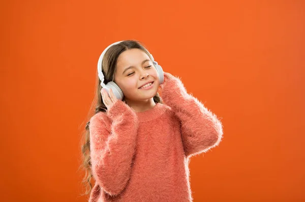 Κορίτσι χαριτωμένο μικρό παιδί φορούν ακουστικά ακούν μουσική. Παιδιά Ακούστε μουσική πορτοκαλί φόντο. Συνιστώμενη μουσική με βάση το αρχικό ενδιαφέρον. Καλύτερες δωρεάν εφαρμογές μουσικής για την κινητή συσκευή σας. Απολαύστε τον ήχο — Φωτογραφία Αρχείου