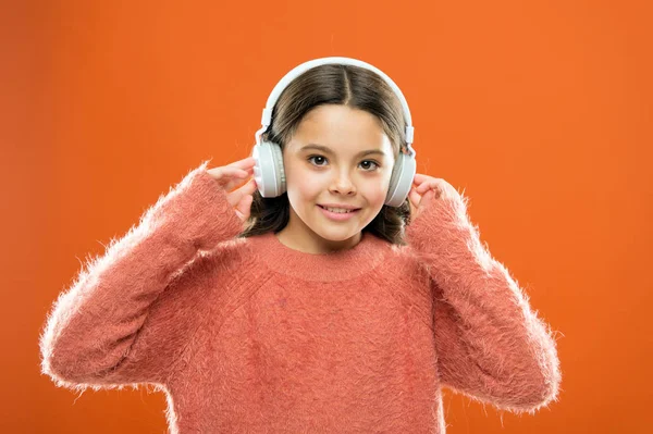 Najlepsze darmowe aplikacje muzyczne dla urządzenia mobilnego. Ciesz się dźwiękiem. Dziewczyna cute little dziecko nosić słuchawki słuchać muzyki. Dziecko słuchać muzyki pomarańczowe tło. Zalecana muzyka na podstawie początkowego zainteresowania — Zdjęcie stockowe