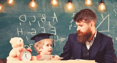 Meşgul bir çocuk okulda okuyor. Öğretmen formal giyim ve öğrenci sınıfta kolej, kara tahta arka plan. Öğretmen, babası ödev, kontrol yardımcı olur çocuk için evlat. Bireysel eğitim kavramı