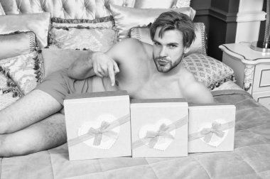 Boks gün vererek hediye. Seksi adam işaret parmağı hediye kutuları, şerit yay ile bağlı. Yakışıklı adam yatakta yatarken kutularında bir şey sunmak. Tatil kutlaması ve hazırlık. Boks günün kutlu olsun