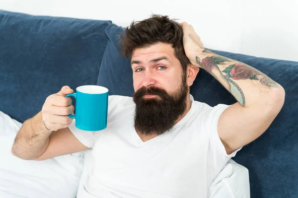 Tune in to new day. Morning awakening better with cup coffee. Relax and rest. Humanity runs on coffee. Man brutal handsome hipster relaxing bedroom drink coffee. Bearded guy enjoy morning coffee