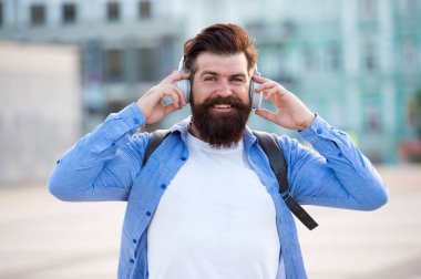 Turist tatili. Hipster modern turistik kentsel arka plan. Sırt çantası kulaklıkile Turist yakışıklı hipster. Sakallı ve sırt çantasıolan adam şehri müzik dinlerken keşfediyor. Seyahat ve macera konsepti