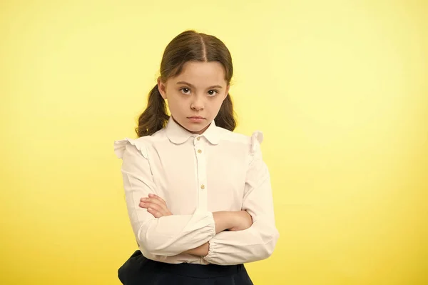 Disagreement and stubbornness. Girl school uniform serious face offended yellow background. Kid unhappy looks strictly. Girl folded arms on chest looks serious. Sensitive girl not want to talk — Stock Photo, Image