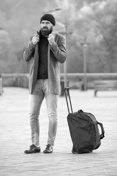 Looking for accommodation. Man bearded hipster travel with big luggage bag wait for taxi bring him to hotel. Travel tips. Traveler with suitcase arrive travel destination. Hipster ready enjoy travel