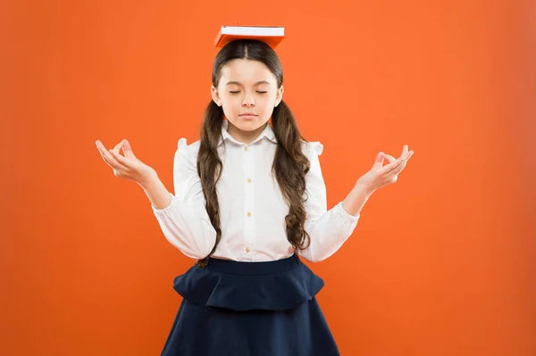 Mediteren altijd. Schattig klein kind leren om te mediteren op oranje achtergrond. Kalm klein meisje mediteren houden boek op hoofd. Mediteren en je verstand begrijpen — Stockfoto