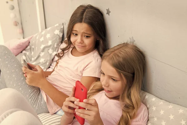 Activities for pajama party. Girls kids best friends or sisters wear pajama busy with smartphones. Children in pajama interact with smartphones. Technologies for kids generation. Pajama party ideas