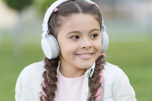 現代のライフスタイル。小さな子供は屋外でモダンな音楽を聴いて楽しみます。夏に近代的なステレオヘッドフォンを着用している小さな女の子。喜びと教育のための近代的な技術の使用 — ストック写真