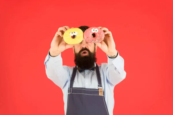 Doces e bolos. Comida de plástico. Hipster barbudo padeiro segurar donuts. Come donut. Humor alegre. Calorias de donut. Donut vitrificado. Homem barbudo e bem preparado com avental a vender donuts. Comida de donut. Produtos de panificação — Fotografia de Stock