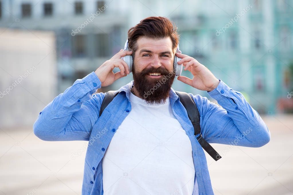 Tourist vacation. Hipster modern tourist urban background. Tourist handsome hipster with backpack headphones. Man with beard and rucksack explore city listening music. Travel and adventure concept