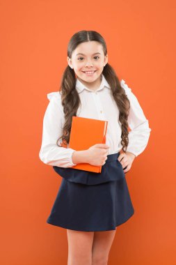 Çocuklar için ilginç bir kitap. Okul üniformalı küçük bir kız. bilgi formu kitap almak. turuncu arka plan üzerine notlar yazma kız öğrenci. Evde eğitim konsepti. mutlu kız için ilginç bir hikaye