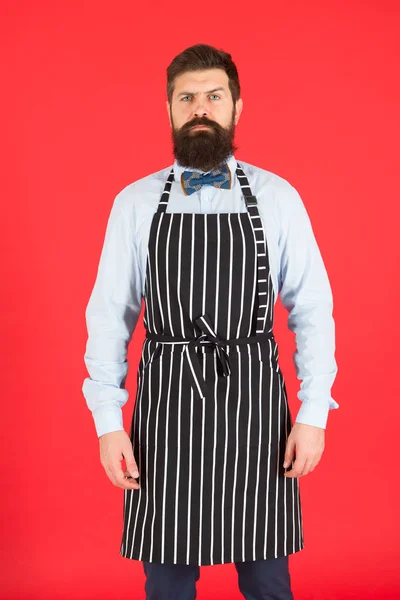 Serveur hipster. Concept de café Hipster. Homme avec barbe cuisinier tablier hipster. Hipster chef cuisinier fond rouge. Un homme barbu cuisinier. Service et personnel du restaurant. Serveur bien entretenu au travail — Photo