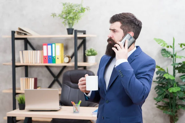 Man bebaarde zakenman Hold Cup en smartphone. Mobiele telefoon. Start dag met koffie. Koffie ontspannen pauze. Baas genieten van energiedrank. Koffie is belofte van succesvolle onderhandelingen. Cafeïne verslaafd — Stockfoto