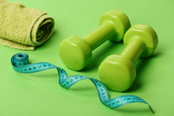 Sports regime symbols. Dumbbells in green color, twisted measure tape