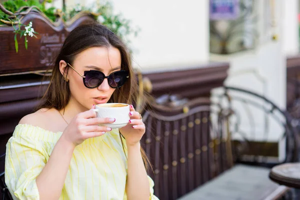 Дівчинка насолоджується ранковою кавою. Жінка в сонцезахисних окулярах п'є каву на відкритому повітрі. Дівчина відпочиває в чашці капучино. Доза кофеїну. Кава для енергійного успішного дня. Чекаю побачення. Час сніданку в кафе — стокове фото