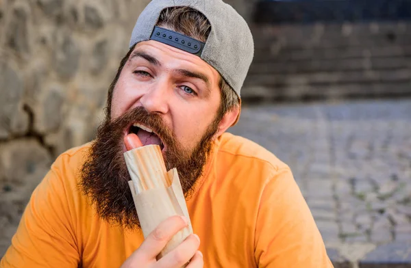 Um lanche de homem faminto. Comida de plástico. Um tipo a comer cachorros quentes. Homem barbudo mordida saborosa salsicha e beber copo de papel. Comida de rua tão boa. Nutrição de estilo de vida urbano. Despreocupado hipster comer junk food while sit on stairs — Fotografia de Stock