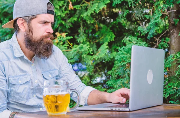 Hipster relax sit terrace with beer. Bearded hipster freelancer enjoy end of working day with beer mug. Beer helps him relax after hard day. Brutal man leisure with beer and laptop. Finally friday