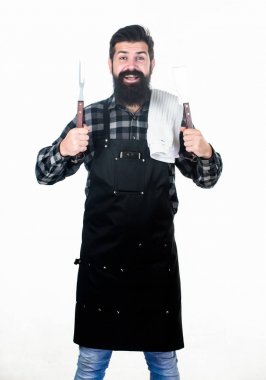 Parkta et pişirmek. Barbekü ustası. Sakallı hipster barbekü için önlük giyer. Kavurma ve ızgara yemeği. Adam pişirme gereçleri barbekü tutun. Açık havada et kavurma araçları. Piknik ve barbekü